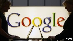 Exhibitors work in front of an illuminated sign of the Google logo in Hanover, Germany